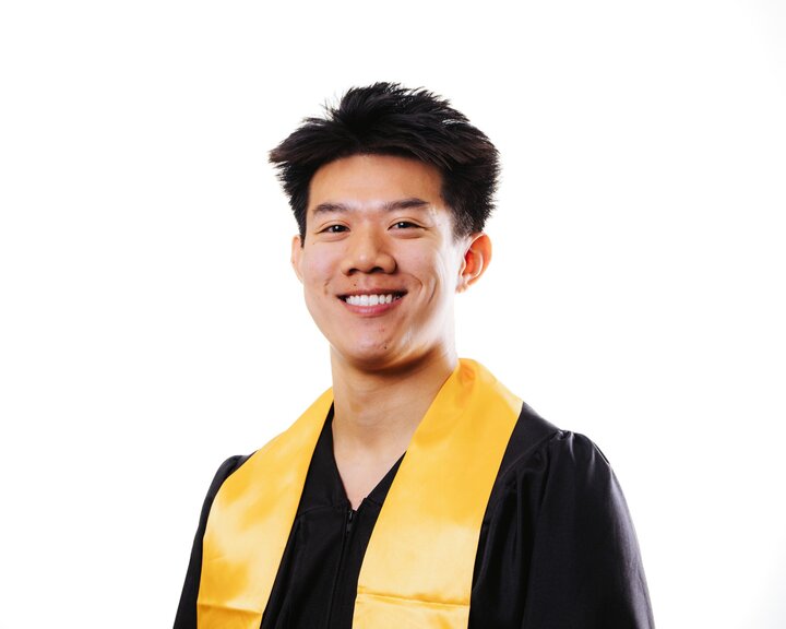Smiling graduate in a black gown and yellow stole, standing against a white background.